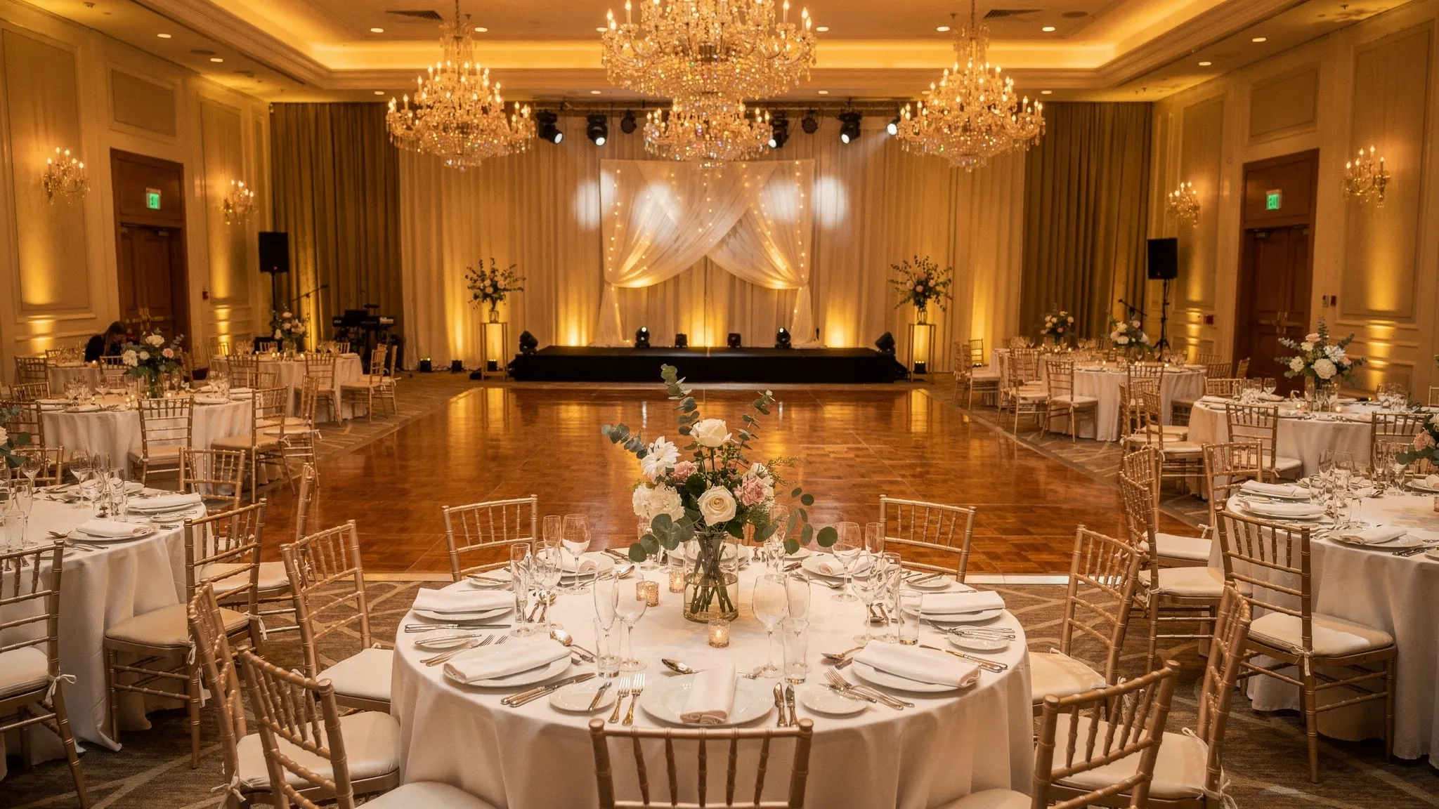 Ballroom events București: cum arată un eveniment premium 2 O sală de ballroom elegantă, pregătită pentru un eveniment premium, cu aranjamente florale moderne, iluminat ambiental cald, mese rotunde impecabil aranjate și ring de dans central.