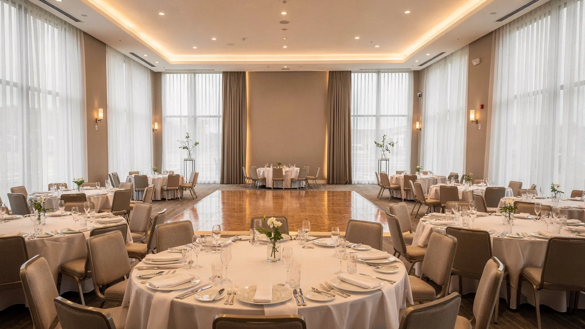 O sală de evenimente modern-elegantă, cu mese rotunde aranjate pentru o petrecere, lumini calde ambientale, zonă de dans liberă și accente de decor minimalist, pregătită pentru un eveniment premium.